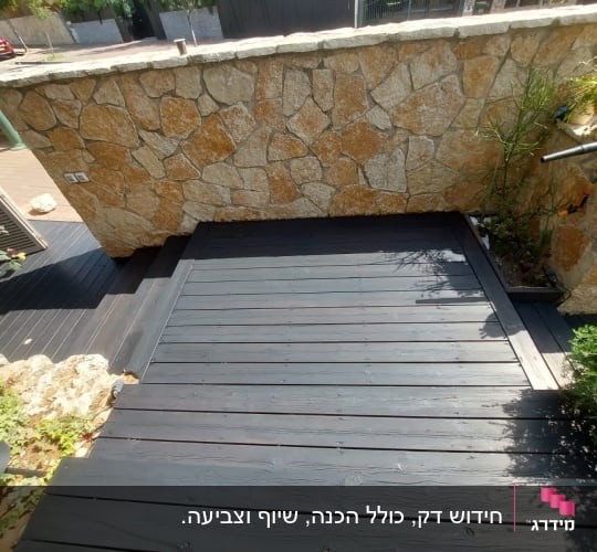 דק עץ כהה ליד קיר אבן בגינה